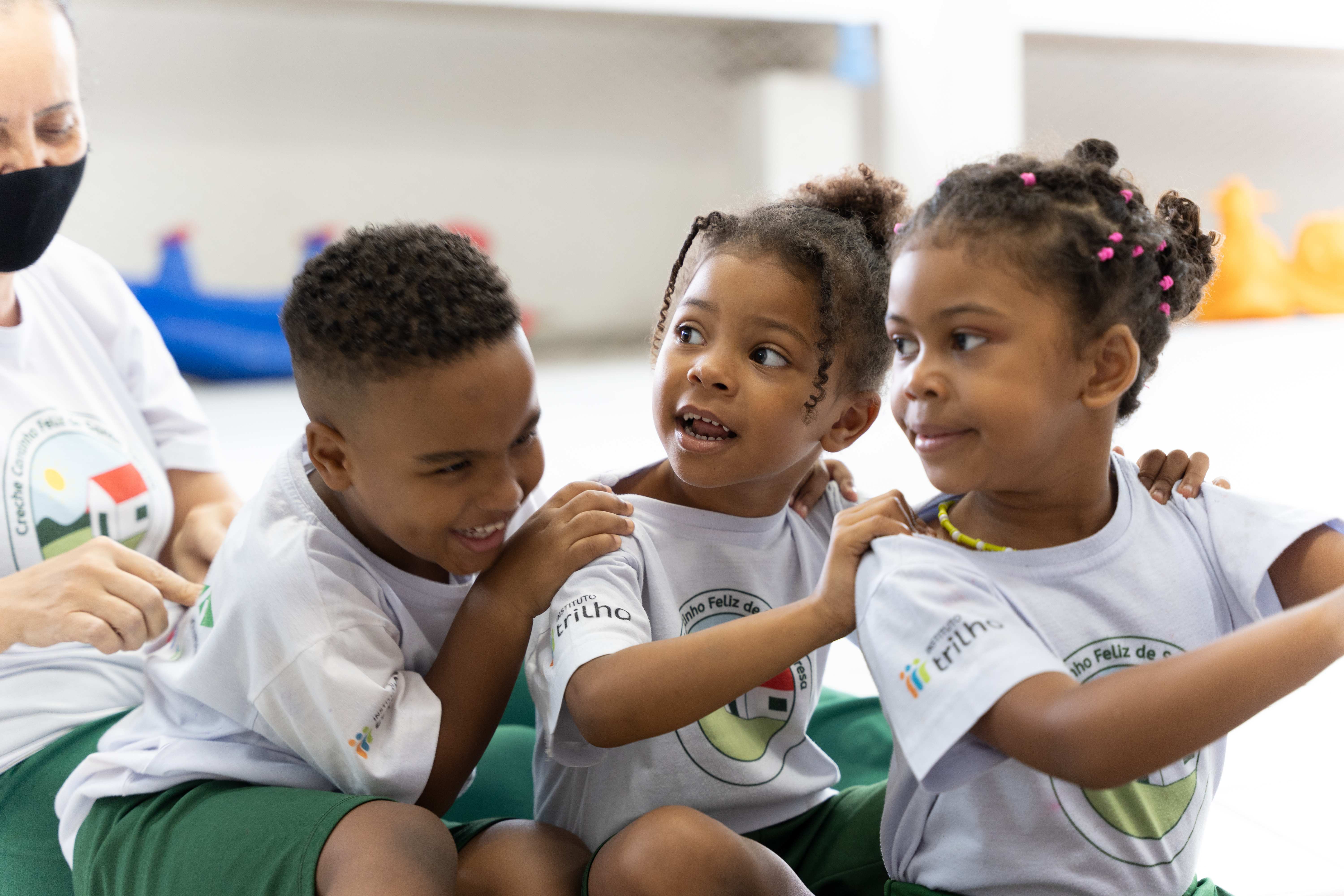 Drei Kinder sitzen lachend hintereinander und fassen sich an den Schultern. (Quelle: Christian Nusch) 
