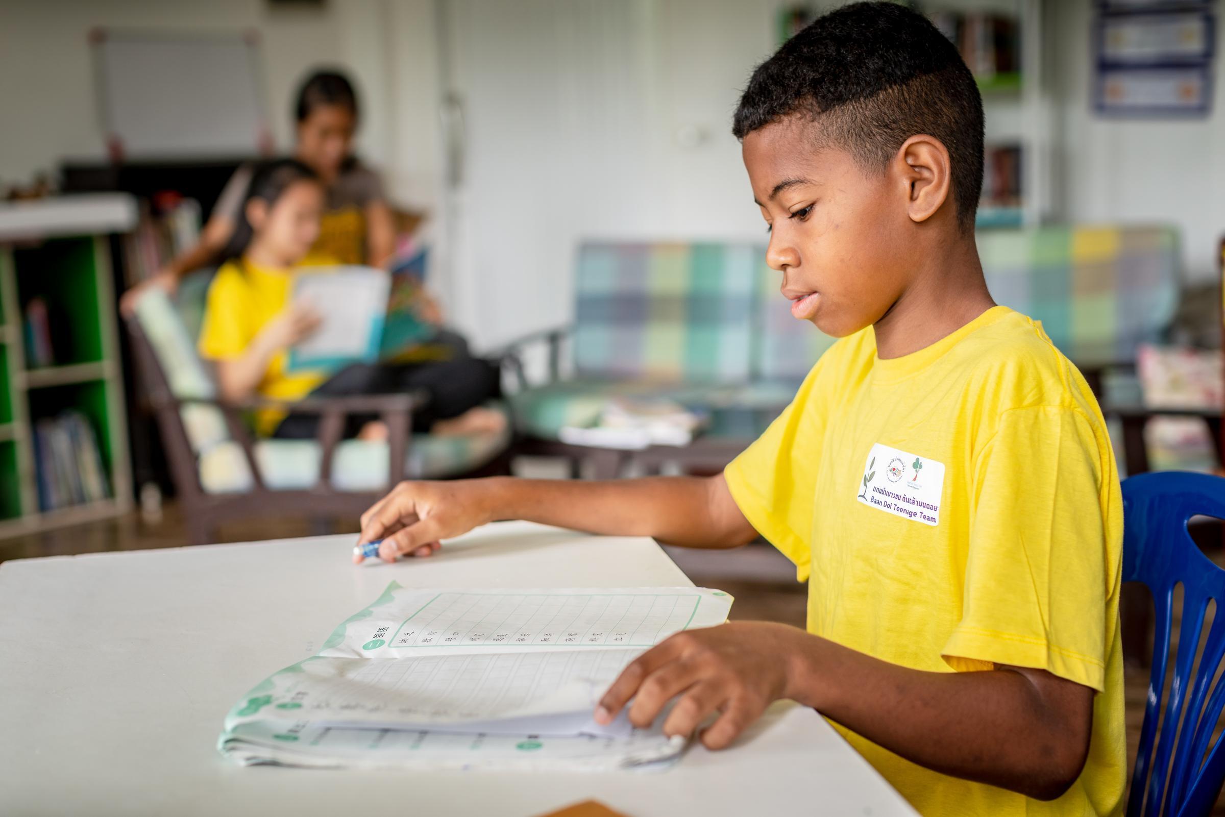 Ein Junge aus Thailand sitzt an einem Tisch und liest in einem Arbeitsheft (Quelle: KNH / Jakob Studnar) Ein Junge aus Thailand sitzt an einem Tisch und liest in einem Arbeitsheft (Quelle: KNH / Jakob Studnar)